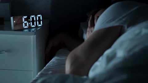 Young man sleeping in bed pressing snooze button on alarm clock at six o'cl.. Stock Footage 289562575