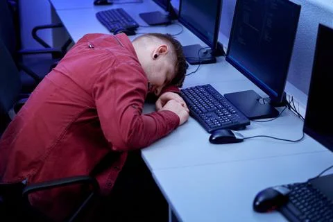 A young man is sleeping at a computer desk. Tired after a long day at work. Stock Photos