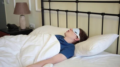 Young man with sleeping mask lying in bed in the morning Stock Footage 70572869
