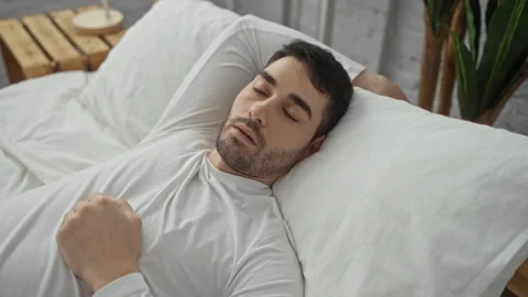 Young man sleeping peacefully in a cozy bedroom on a white bed with a seren.. Stock Footage 310031265