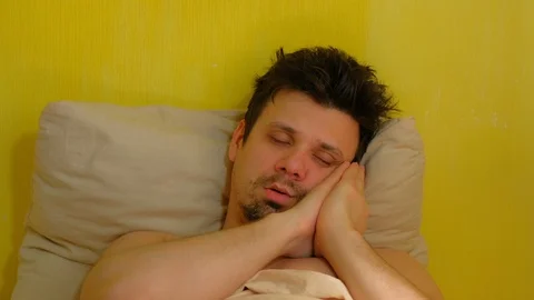 Young man is sleeping in reclining pose with hands on face and snores. Video stock 128952229