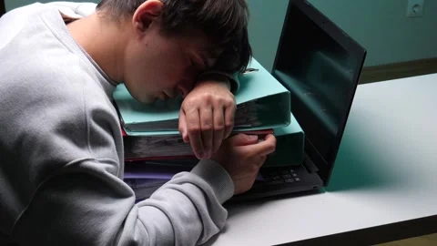 Young man sleeping on a stack of binders and documents next to a laptop Stock Footage 346250417