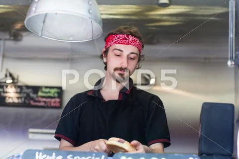 Young Man Slicing Hamburger Bread Roll On Fast Food Van