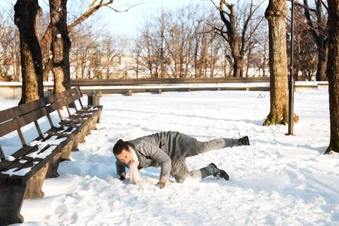 Young man slipping and falling on snow in a winter park. Clumsy guy stumbli.. Stock Photos