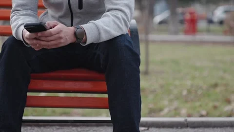 Young man with smart watch using smartphone sits on bench in city park Stock Footage 321359207