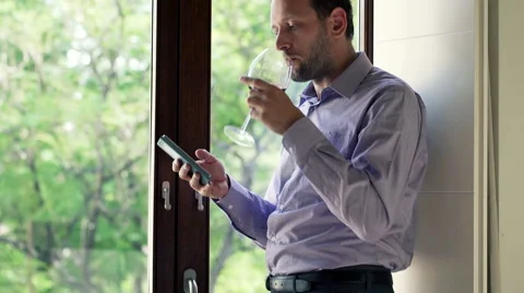 Young man with smartphone and wine standing by the window HD Stock Footage 44793886