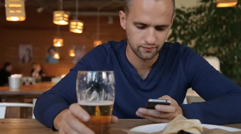 Young man with smartphone drinking beer in cafe Stock Footage 67861617
