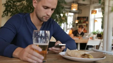 Young man with smartphone drinking beer in cafe Stock Footage 67861668