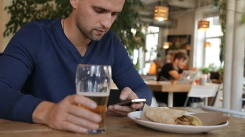 Young man with smartphone drinking beer in cafe Stock Footage 67861772