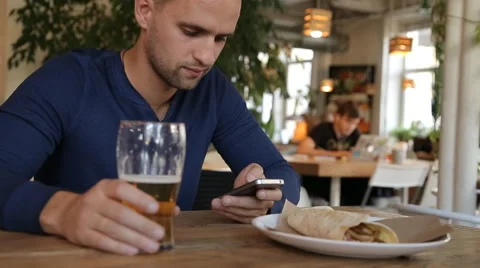 Young man with smartphone drinking beer in cafe Stock Footage 67861828