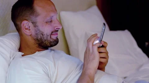 Young man with smartphone lying on bed during night Stock Footage 103264897
