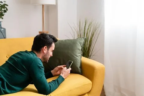 Young man with smartphone lying on sofa Stock Photos