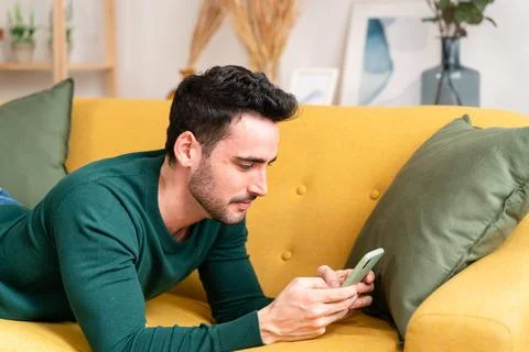 Young man with smartphone lying on sofa Stock Photos