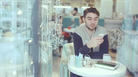 Young man with smartphone sitting in cafe 스톡 동영상 58645528