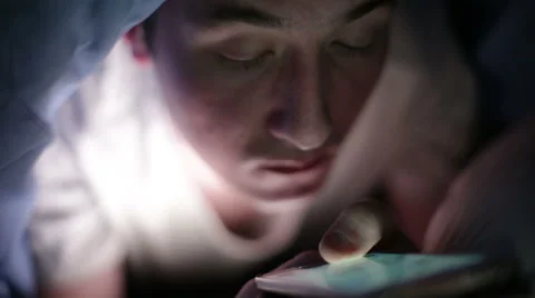 Young Man On Smartphone Under Bed Sheets Stock Footage 49893992