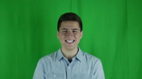 Young man smiles and laughs in a blue shirt in front of a greenscreen Vidéo 59088802