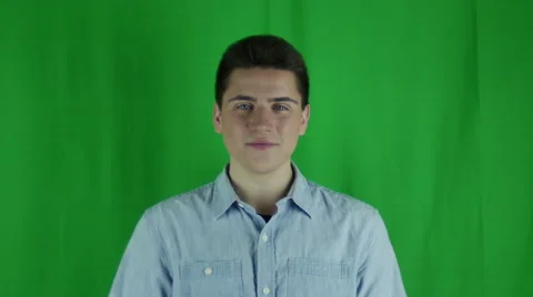 Young man smiles and waves enthusiatically in front of greenscreen Stock Footage 59087835