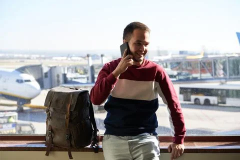 Young man smiles confident while talking on his phone from the airport Stock Photos