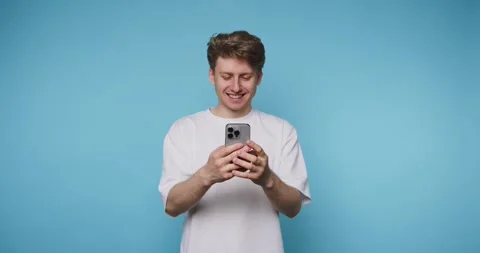 Young man smiles joyfully while looking at his smartphone, showcasing his e.. Stock Footage 313280613