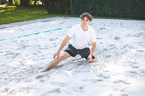 Young man smiles while sitting in the sand after a volleyball play on a sandy Stock Photos
