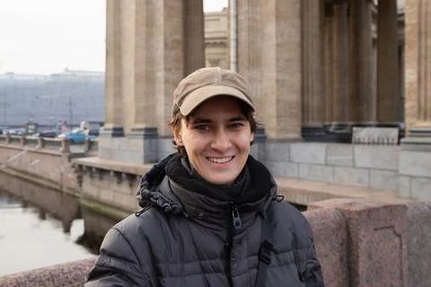 Young man smiles while standing on a bridge in a city with architecture Stock Photos