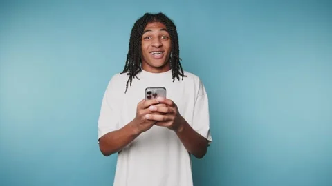 Young man smiles while using smartphone against a blue background during a .. Stock Footage 313273961