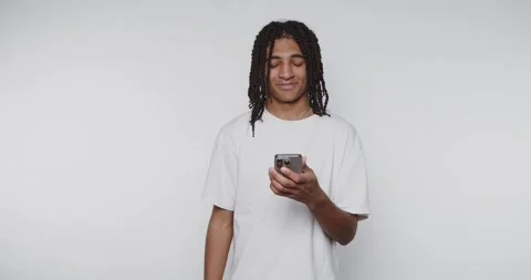 Young man smiles while using smartphone in a plain room during after school.. Stockbeeldmateriaal 328248588