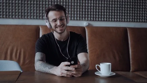 Young man smiling and nodding with the music in his headphones holding his Stock Footage 106093470