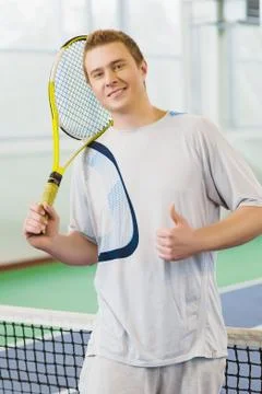 Young man smiling and posing with tennis racket indoor Stock Photos