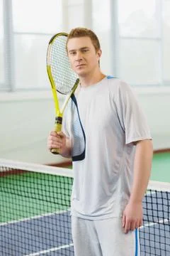 Young man smiling and posing with tennis racket indoor Stock Photos