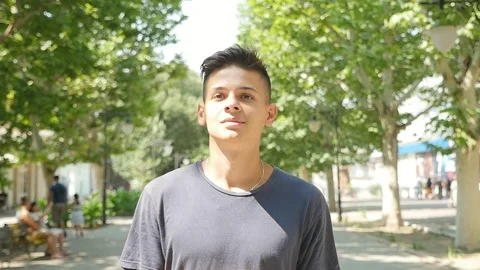 Young man is smiling and strolling along a park alley in summer in slow motion Stock-Footage 96141735