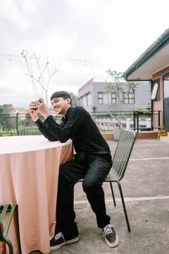 Young man smiling and using a camera while sitting at outdoor cafe Stock Photos