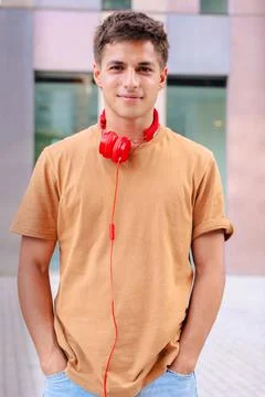 Young man smiling at camera with red headphones around neck in urban setting Stock Photos