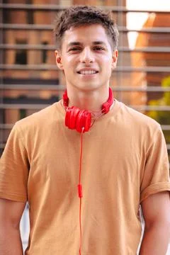 Young man smiling at camera with red headphones around neck in urban setting Stock Photos