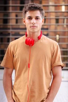 Young man smiling at camera with red headphones around neck in urban setting Stock Photos