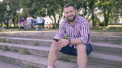 Young man smiling for camera, sitting on stairs. Slider and pan shot. Vídeo Stock 67241466
