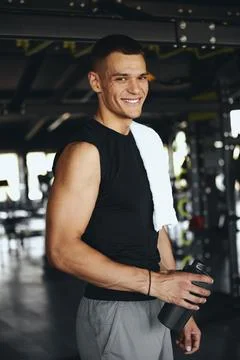 Young man smiling confidently while holding sports shaker in gym during his Stock Photos