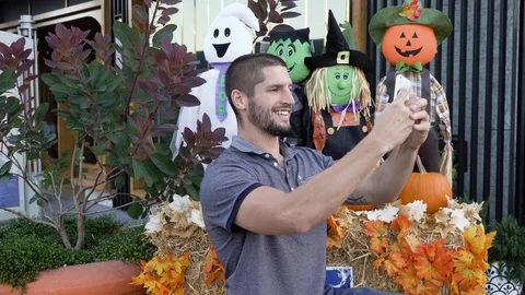 Young man smiling posing for selfie in front of halloween scarecrow decor Stock Footage 118672763