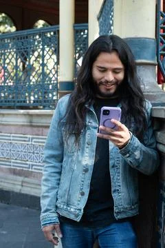 Young man smiling using smartphone outdoor with long hair Stock Photos