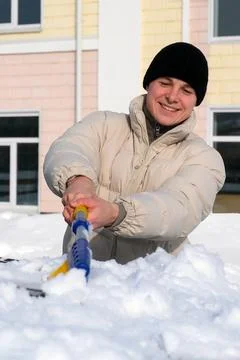 Young man smiling while brushes thick snow and ice off a parked car on a br.. Stock Photos
