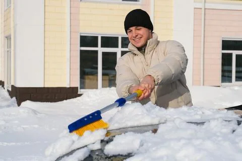 Young man smiling while cleaning snow from car hood in city winter morning .. Stock Photos