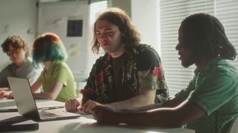 Young Man Smiling while Discussing Data on Laptop with Coworker in Office 動画素材 340486343