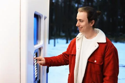 A young man smiling while interacting with a modern, white and blue vending.. Stock Photos