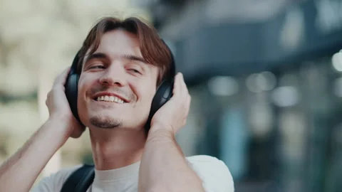 Young man smiling while listening to music with headphones on city street Stock Footage 339215460
