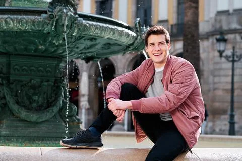 Young man smiling while sitting outdoors in a water fountain. Stock Photos