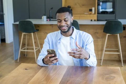 Young man smiling while talking on his smartphone in a modern kitchen, enjo.. Stock Photos