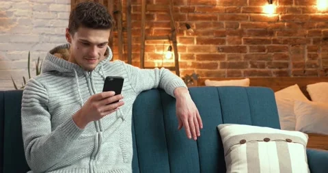 Young Man smiling while using his Phone, ordering Porterage at Home. Attractive Stock Footage 130353223