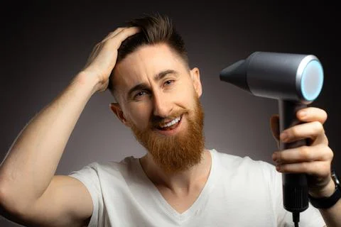 Young man smiling while using hair dryer isolated over black background Stock Photos