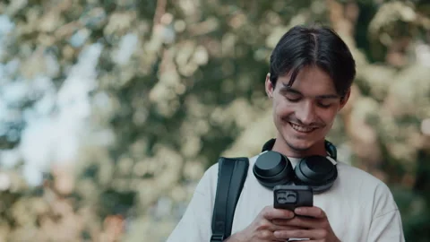 Young man smiling while walking outdoors using phone Stock Footage 339216127