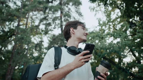 Young man smiling while walking in park, drinking coffee and using phone Stock Footage 339216205